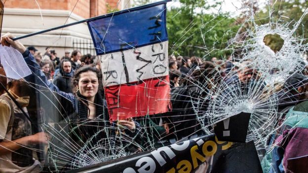A protester holds the French Tricolour with an anti-Macron slogan outside a destroyed McDonald's A protester holds the French Tricolour with an anti-Macron slogan outside a destroyed McDonald's