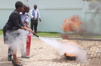 Mr Micheal Obimpeh, the Assistant Station Officer, assisting Ms Philomena Woolly, the Deputy Registrar, Nursing and Midwifery Council, to quench fire in a demonstration Mr Micheal Obimpeh, the Assistant Station Officer, assisting Ms Philomena Woolly, the Deputy Registrar, Nursing and Midwifery Council, to quench fire in a demonstration
