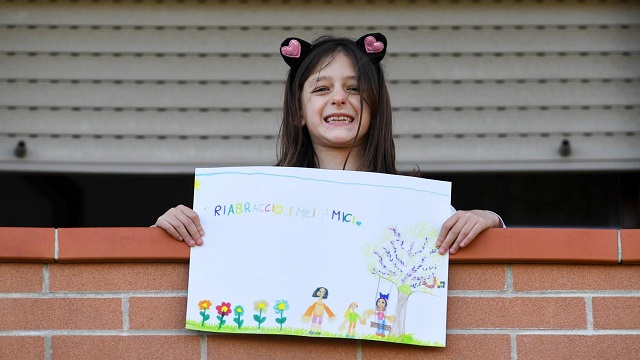 A girl on a balcony poses with a picture she drew (Credit: Reuters) How Covid-19 is changing the world’s children