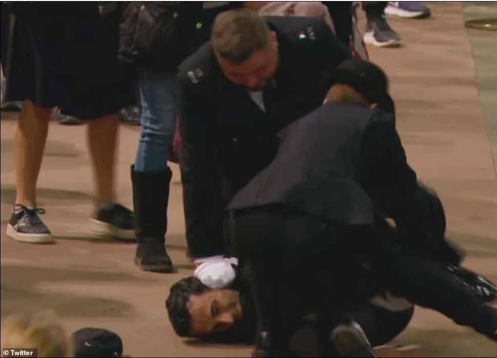 The man who grabbed the Standard smirks as he is held to the floor by police who had dragged him away from the coffin Queen Elizabeth's coffin raider's 'silence' in the queue