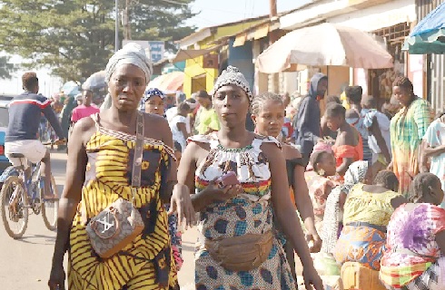 Women walking past people shopping at a market in Bissau