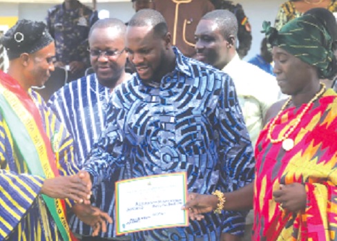 Anwel Sadat Ahmed (2nd from right), MCE for Oforikrom, being assisted by Oheneyere Hoahi Akosua Asamoah II (right), Queenmother of Boadi, to present a certificate to Alhassan Musa Kpabi (left), Best Farmer for the Oforikrom Municipality. With them are other officials of the assembly