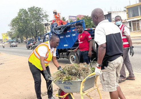 Adamu Musa Kalamu (left), MCE for Ablekuma North, assisting one of the workers to collect some weeds cleared during the exercise