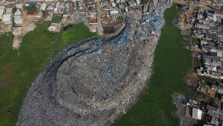 An aerial photograph of a roughly 4-year-old textile dump site in Glefe, inside the Densu Delta protected wetlands, outside Accra, Ghana. The dump site sits close to lagoons and streams, with no lining and no other visible pollution mitigation systems. An aerial photograph of a roughly 4-year-old textile dump site in Glefe, inside the Densu Delta protected wetlands, outside Accra, Ghana. The dump site sits close to lagoons and streams, with no lining and no other visible pollution mitigation systems.
