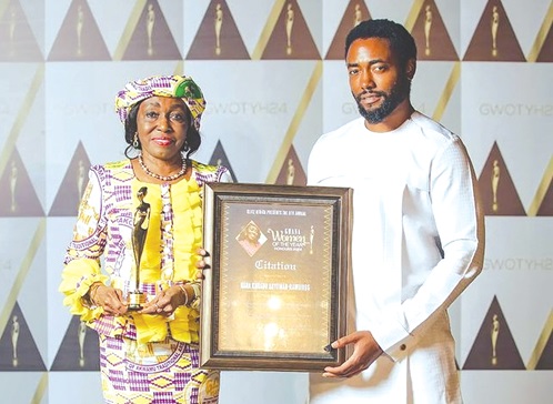 Nana Konadu Agyeman-Rawlings, former First Lady, being assisted by her son, Kimathi Agyeman-Rawlings, to display an award she received