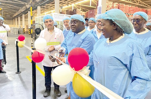 Julius Debrah (2nd from right), Chief of Staff, being assisted by Elizabeth Ofosu-Adjare (right), Minister of Trade, Agribusiness  and Industry, to cut a ribbon and commission the upgraded canmaking line. With them are some officials of Nutrifoods