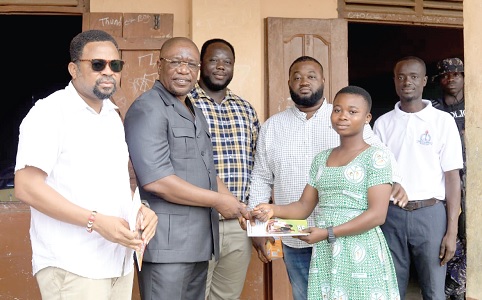 Bright Asamoah Brefo (2nd from left), the MP for Bibiani-Anhwiaso-Bekwai, presenting an exercise book to a pupil, while other officials look on