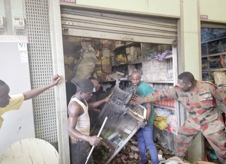 Some men assisting fire personnel to pull out a lockable glass showcase, stockpiled with deodorants, where the fire started