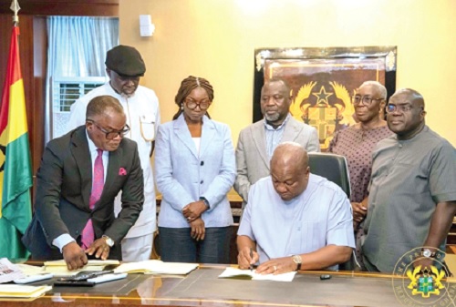 President John Dramani Mahama (seated) signing the documents. Looking on are some government officials