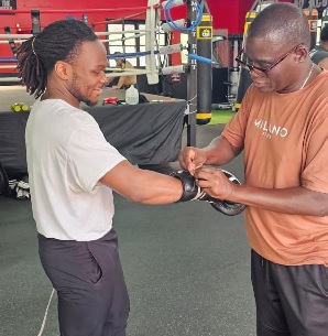 The legendary trainer, Daniel Odamtten (right) helping his boxer to put on his gloves before working on the punching bag