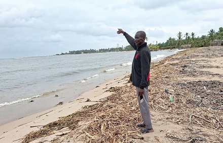 Noah Aggrey, a fisherman, pointing far away to where the shoreline used to be