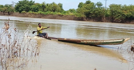 Doutey Mark, a fisherman, paddling a canoe to inspect his nets on the White Volta River