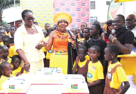Mrs Jeanette Ndhlovu (holding microphone), about to cut a cake to commemorate the 95th birthday celebration of Nelson Mandela with pupils of Baba Yara Primary School at Madina