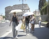 People using umbrellas in hot weather to shelter from the sun while walking past the Colosseum, in Rome