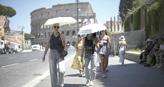 People using umbrellas in hot weather to shelter from the sun while walking past the Colosseum, in Rome