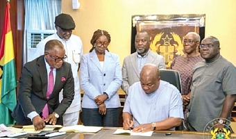 President John Dramani Mahama (seated) signing the documents. Looking on are some government officials